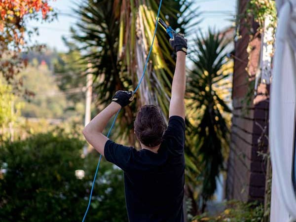 An electrician reaching up to pull cable through beside a house