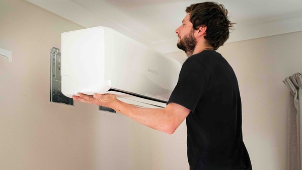An installer lifting a high wall heat pump indoor unit onto its wall bracket in an Auckland home