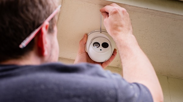 An electrician fitting a white dome security camera into a ceiling.