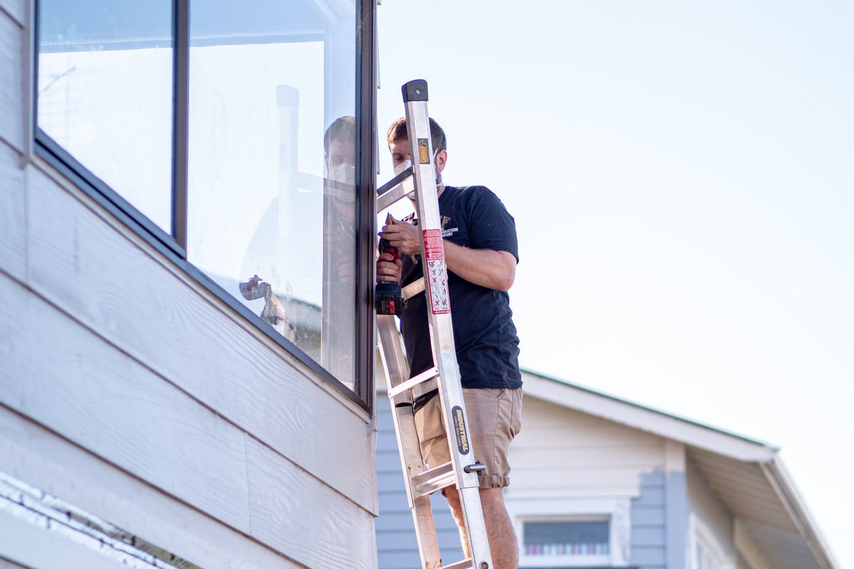 An electrician on a ladder working at the soffit of a two storey weatherboard house.