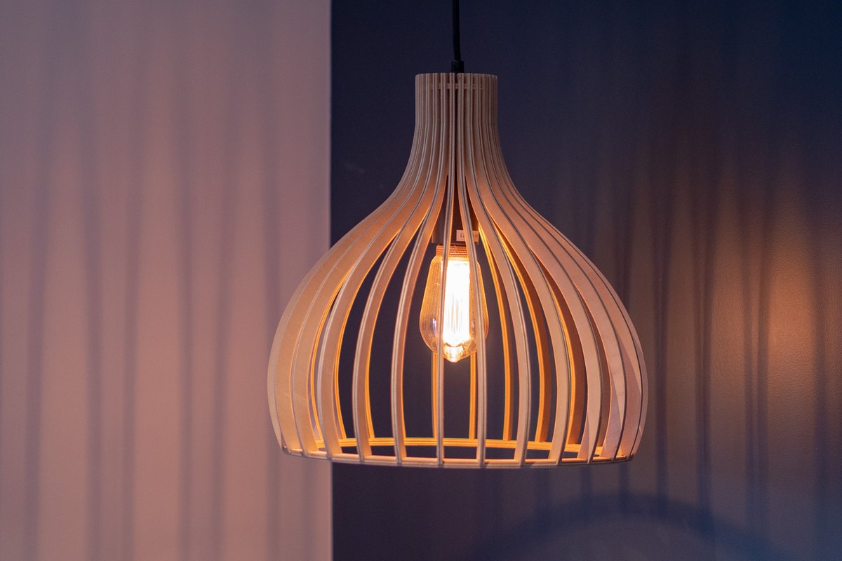 A slatted timber pendant light switched on against a dark blue wall, filament bulb glowing.