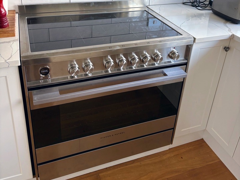 A freestanding stainless steel induction range fitted between white cabinets in a tiled kitchen