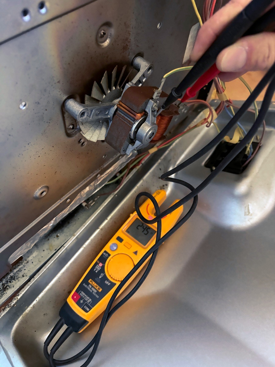 Test probes on the fan motor terminals at the back of an oven, with the tester lying on the metal casing