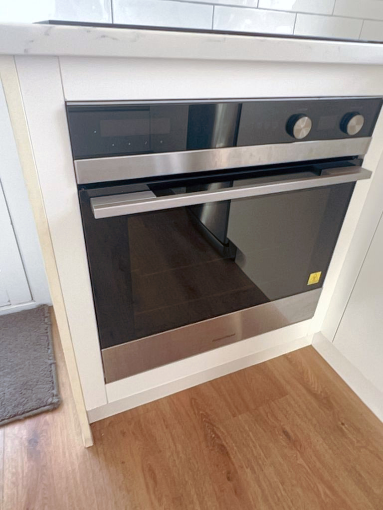 A stainless steel built-in oven fitted under the bench in white cabinetry, with a timber floor