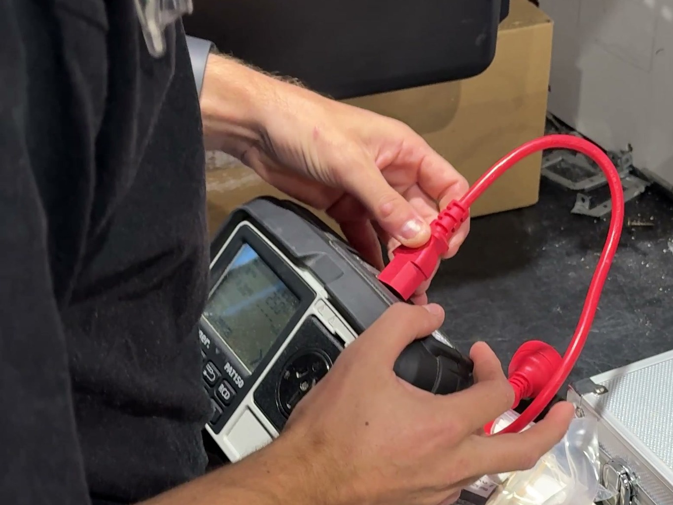 A red test lead being plugged into a portable appliance tester on a workbench
