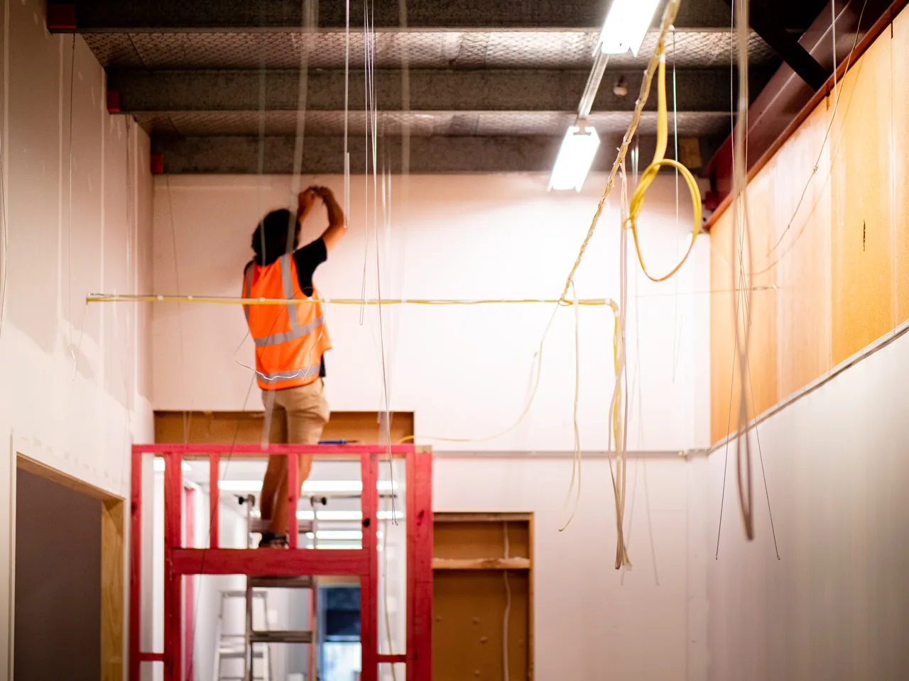 Electrician on a raised platform running cable along the ceiling of a commercial unit being fitted out