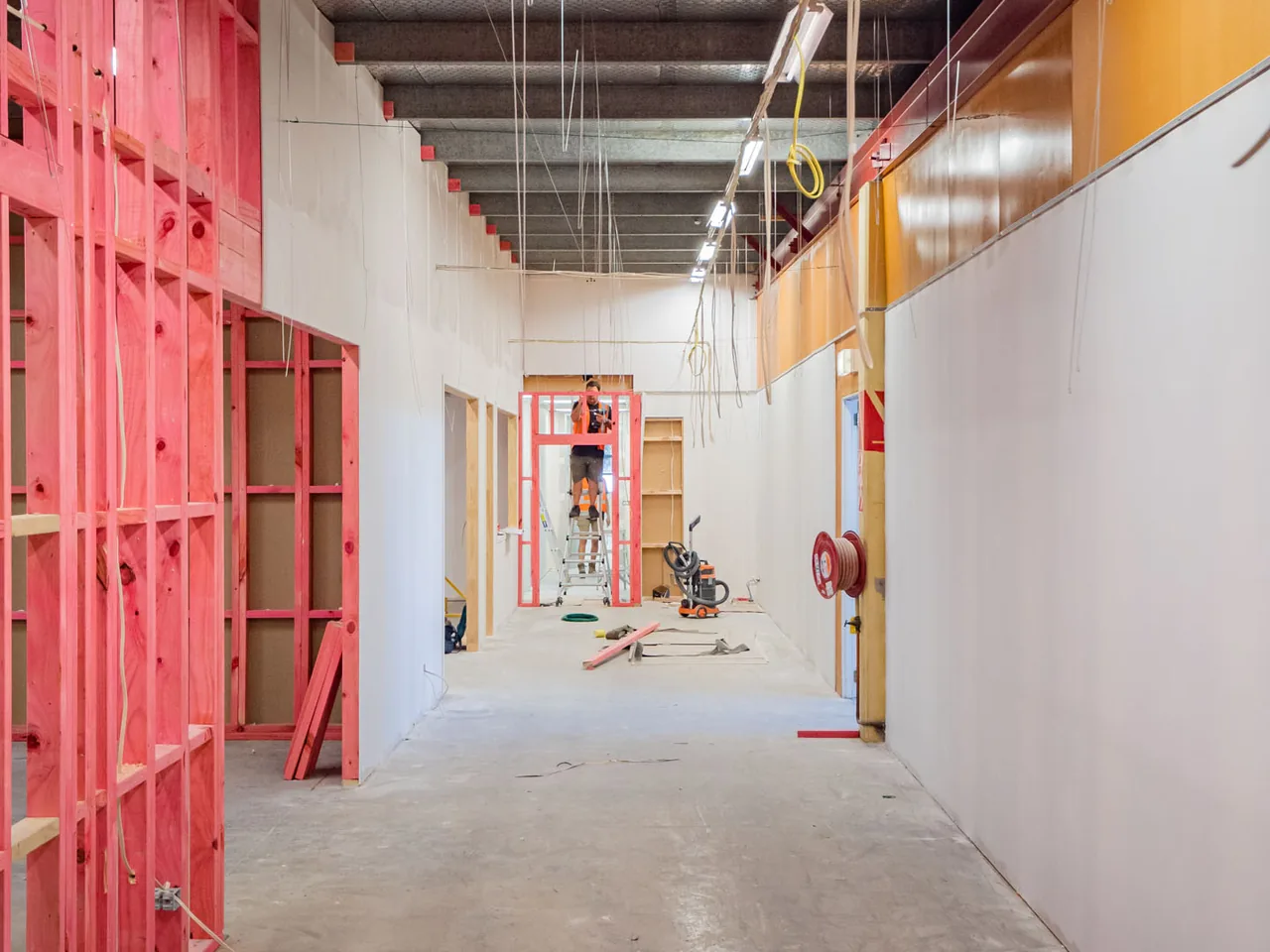 Corridor through a commercial fitout with cabling dropped through the ceiling and a worker on a scaffold at the far end