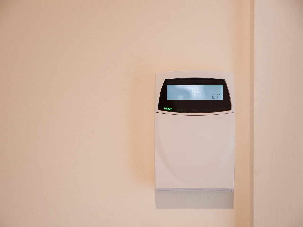 Alarm keypad fixed to a painted wall, its display lit and the ready light on