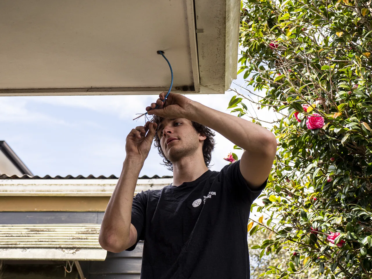 Electrician preparing a blue network cable that comes down through the soffit of a house