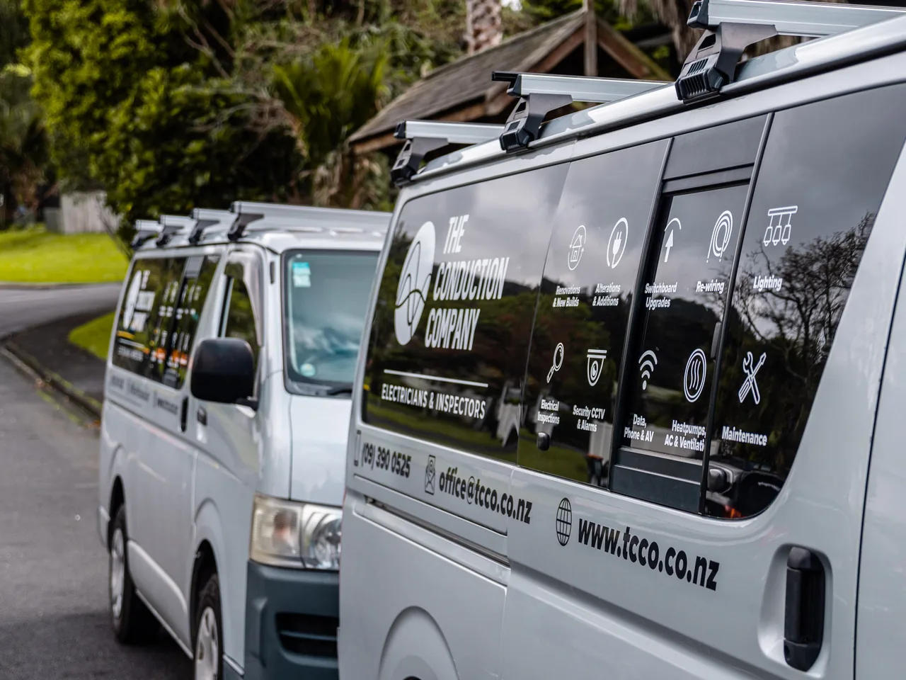 Two signwritten service vans with roof racks parked one behind the other on a suburban street