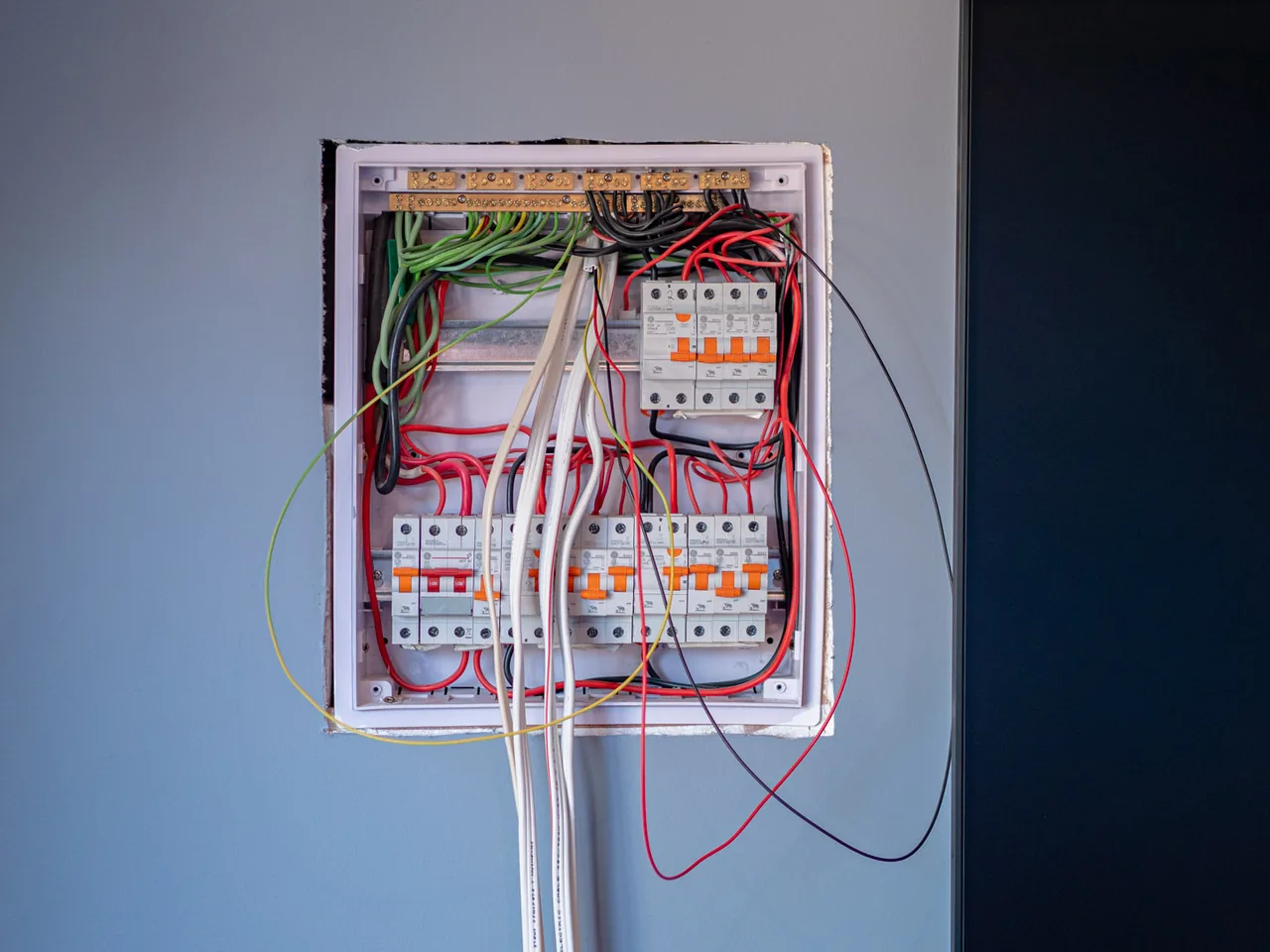 A new switchboard set into a painted wall with its cover off and cables still hanging below