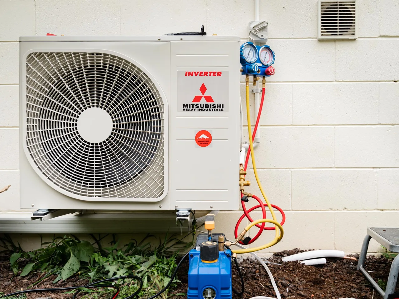 Outdoor heat pump unit against a block wall, connected to refrigerant gauges and a vacuum pump