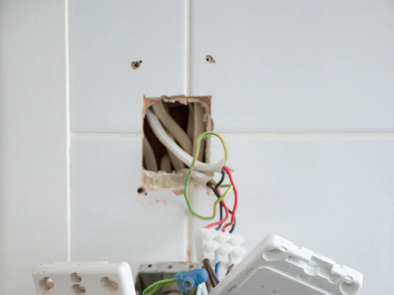 Old wiring exposed in a hole in a tiled wall after the switch plates were taken off, with a connector block below