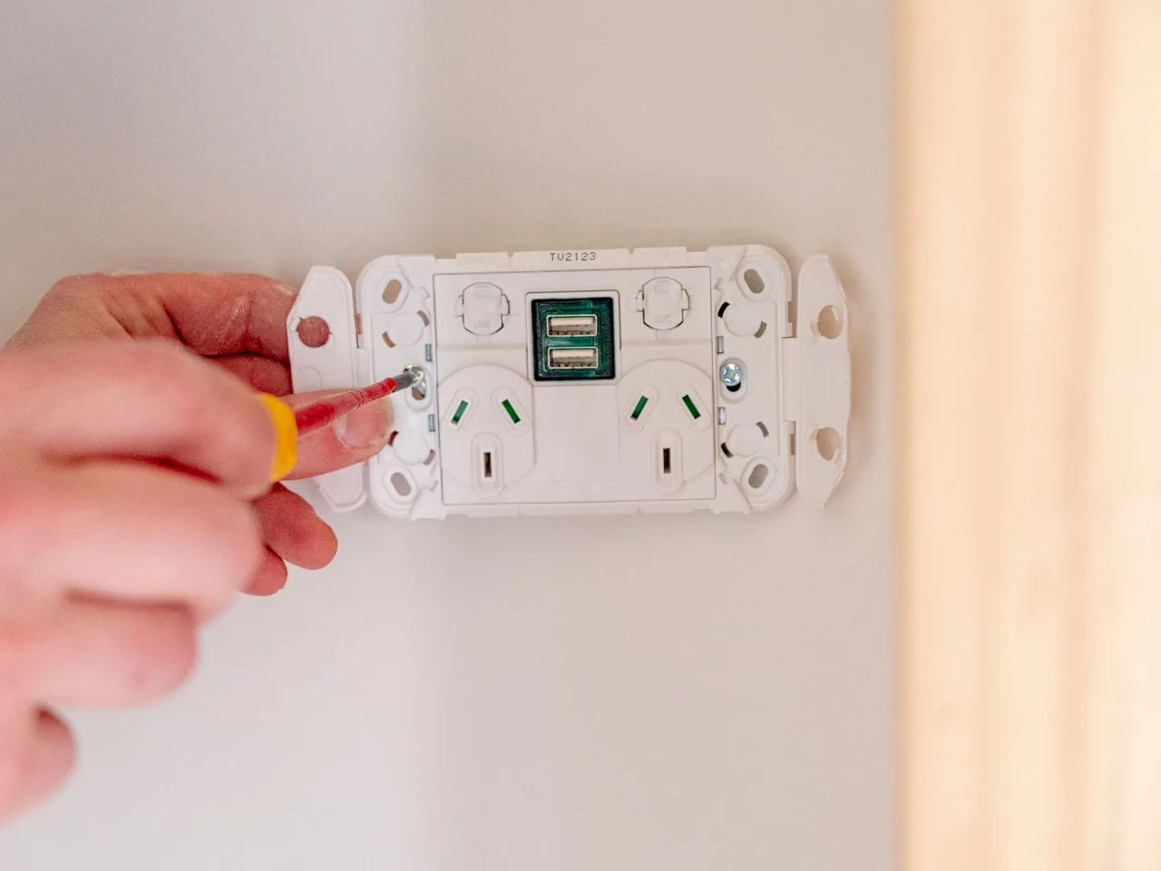 Hand screwing a new double power point with USB charging ports onto a wall