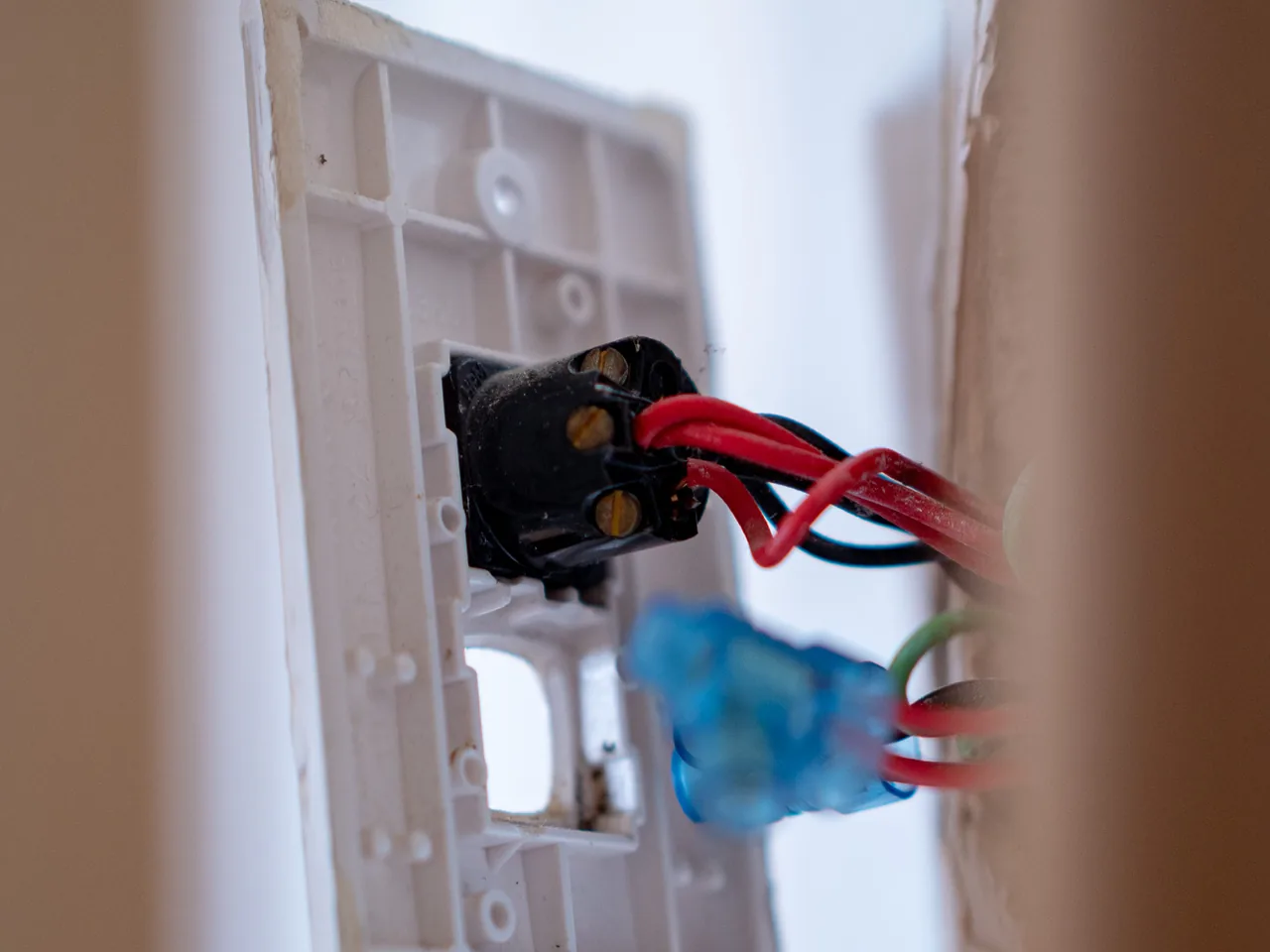 An old light switch pulled from the wall on its cables, red and black conductors and a blue connector behind it