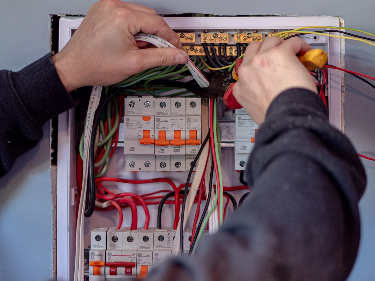 Two hands inside an open switchboard, one holding cables clear while the other tightens a terminal