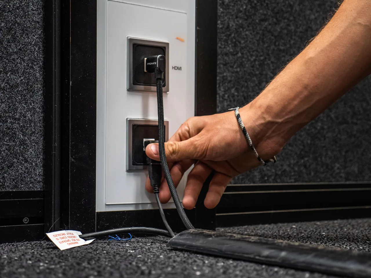 Hand plugging a cable into an HDMI wall plate low on an office wall