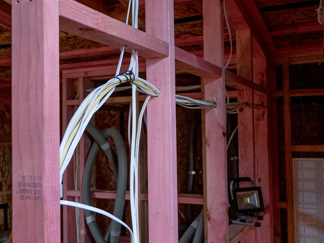 Bundled cables tied to a stud in open timber framing, with grey conduit running behind them