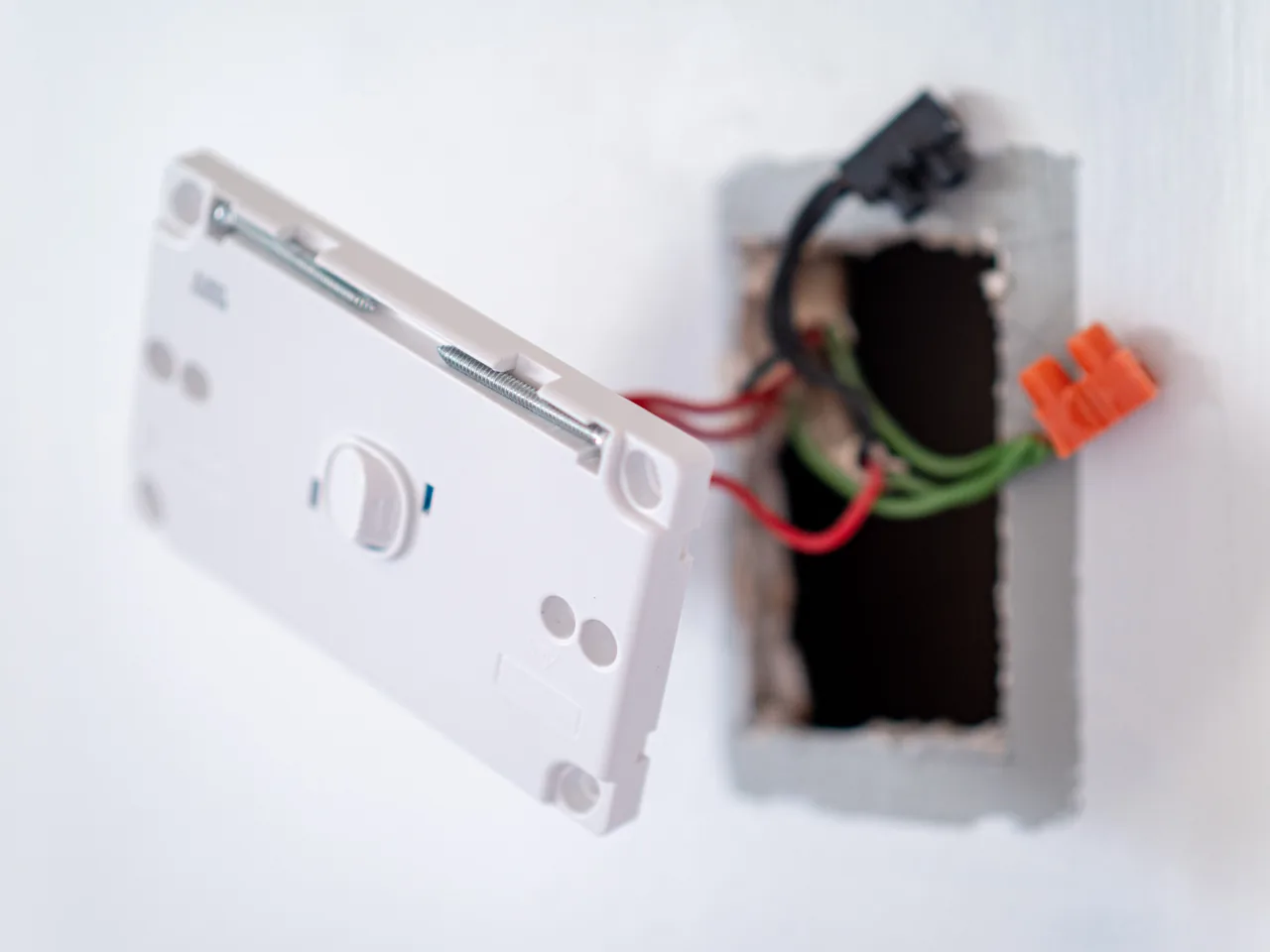 A white rotary wall controller hinged out of its box, showing the red, black and green conductors behind it