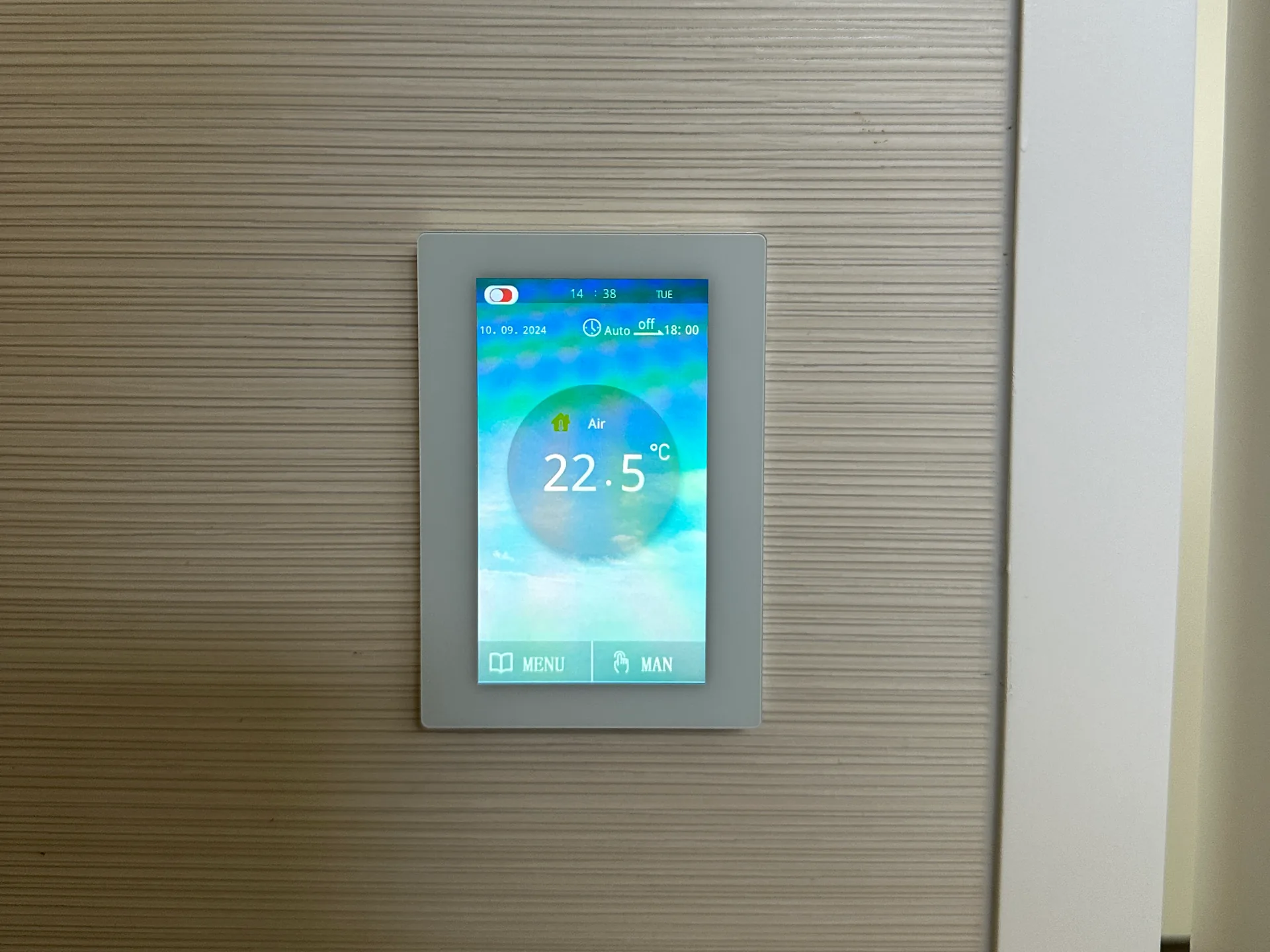 Touch screen floor heating thermostat reading 22.5 degrees on a striped grey wall panel beside a door frame