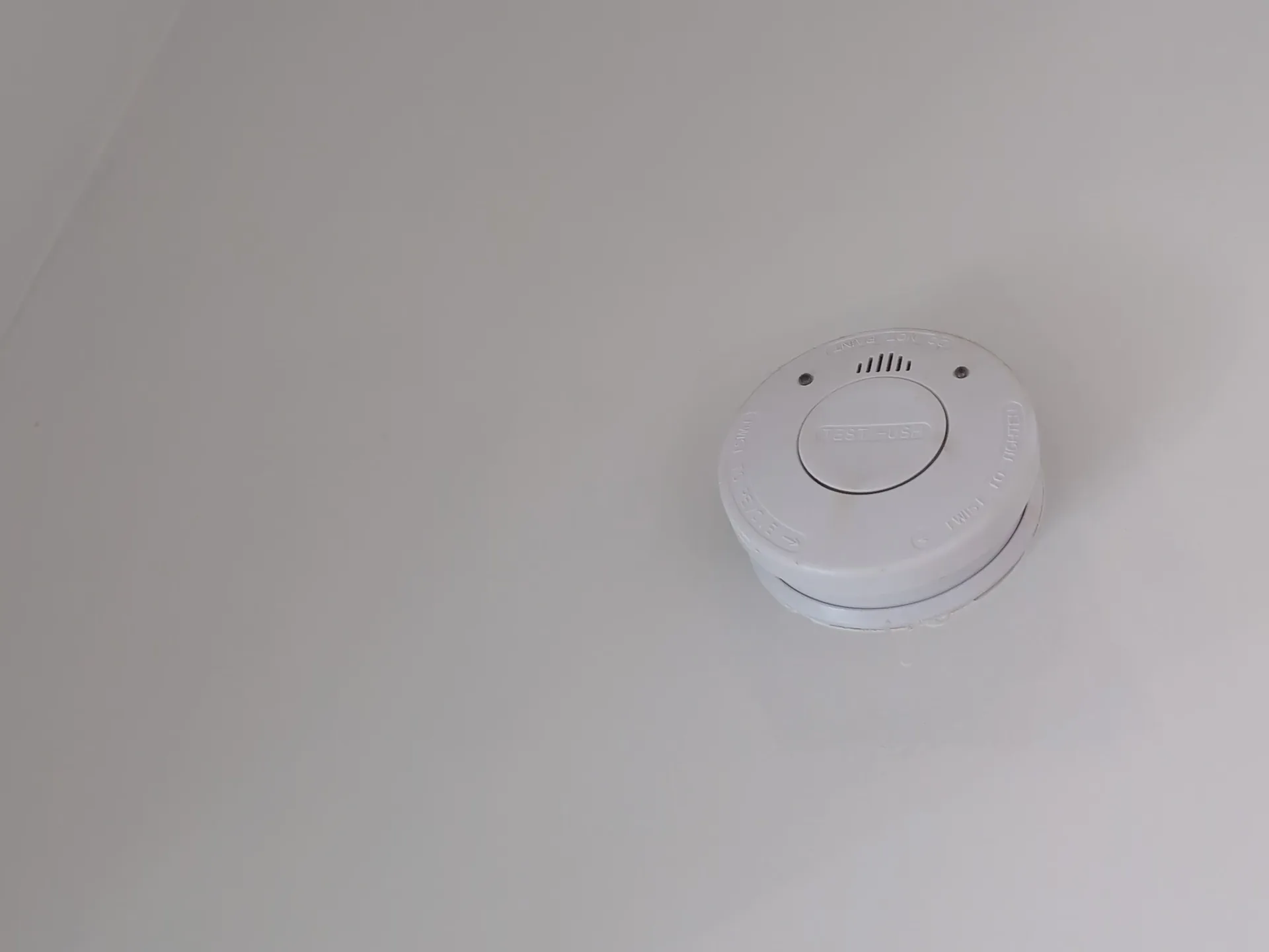 White smoke alarm fitted to a plain white ceiling near the cornice
