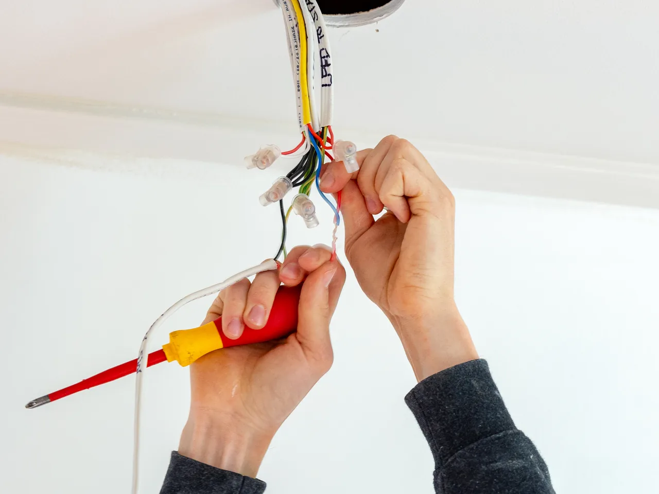 Gloved hands terminating the conductors of a new cable coming out of a ceiling hole
