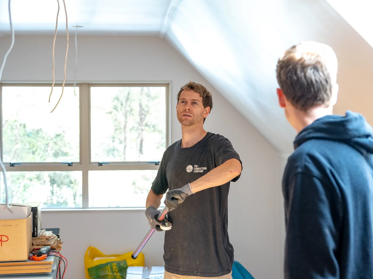 Electrician holding a clamp meter while checking the existing wiring in an attic room
