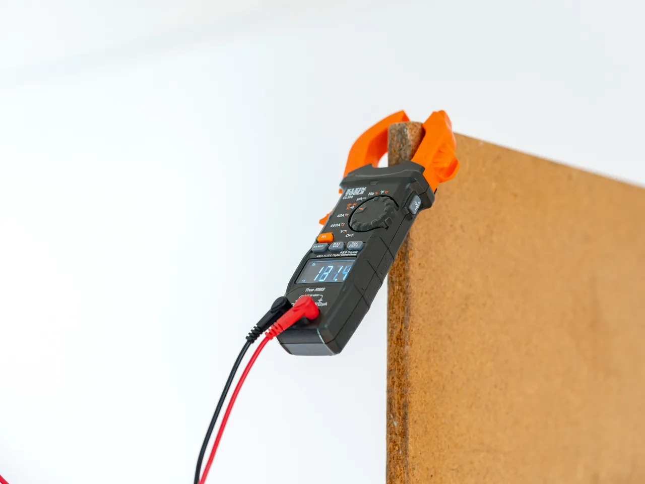 Digital clamp meter clipped to a panel edge showing a live test reading