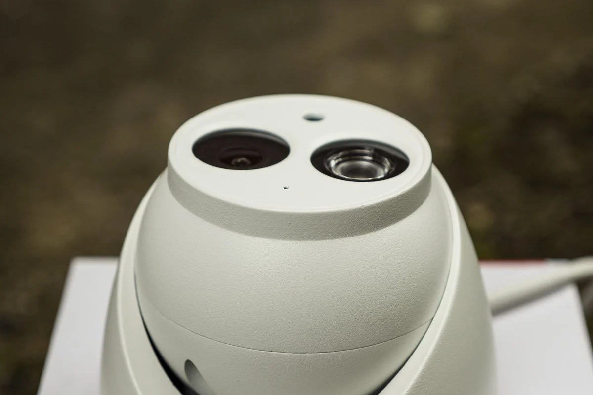 A white dome security camera on a plain surface, lens and infrared sensor sharp, dark background.