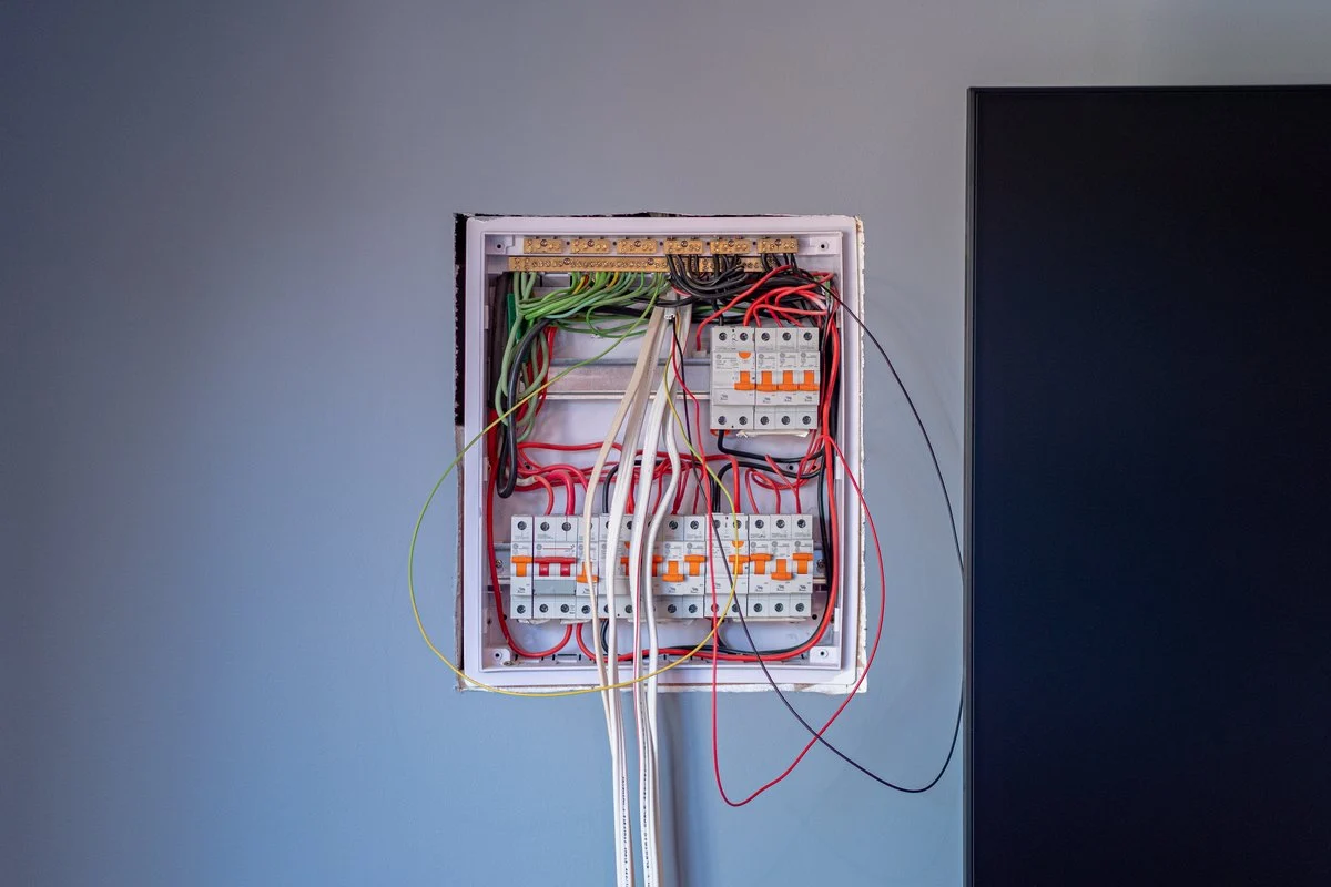 An open domestic switchboard, cover off: rows of circuit breakers and RCDs, neat wiring, white tails down the wall.