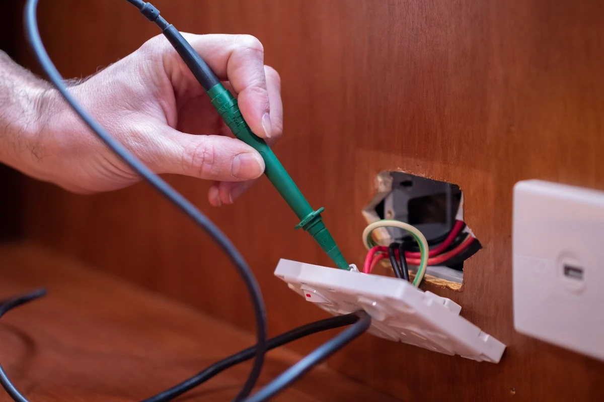 A test probe into the back of a wall plate pulled off a timber wall, a data outlet beside it.
