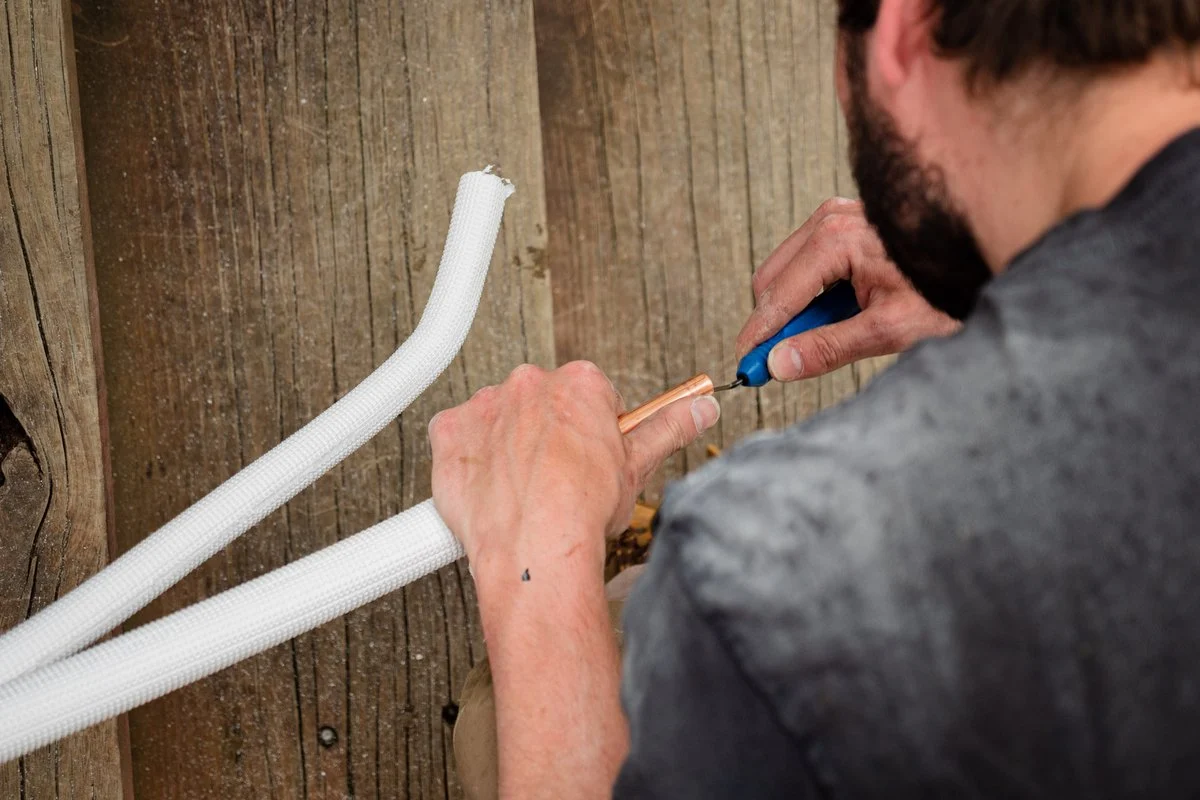 Working a hand tool on a copper flare joint where insulated pipe lines meet.