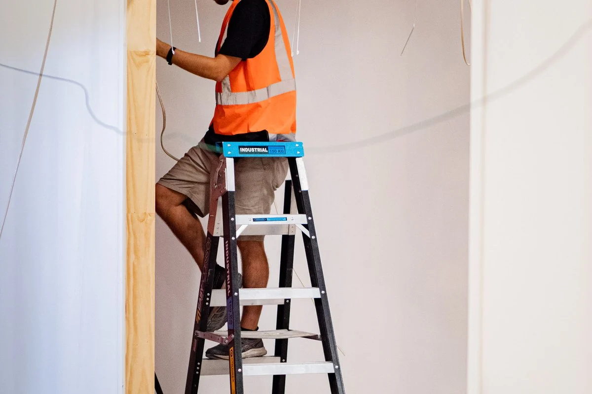 A worker on a step ladder in a doorway, working on cabling above the door head.