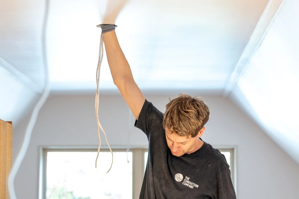 An arm fully extended, pulling white cable down out of a ceiling hole.
