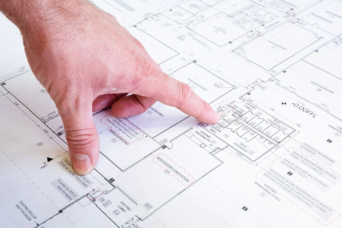 A hand pointing at a detail on a large architectural and services drawing.