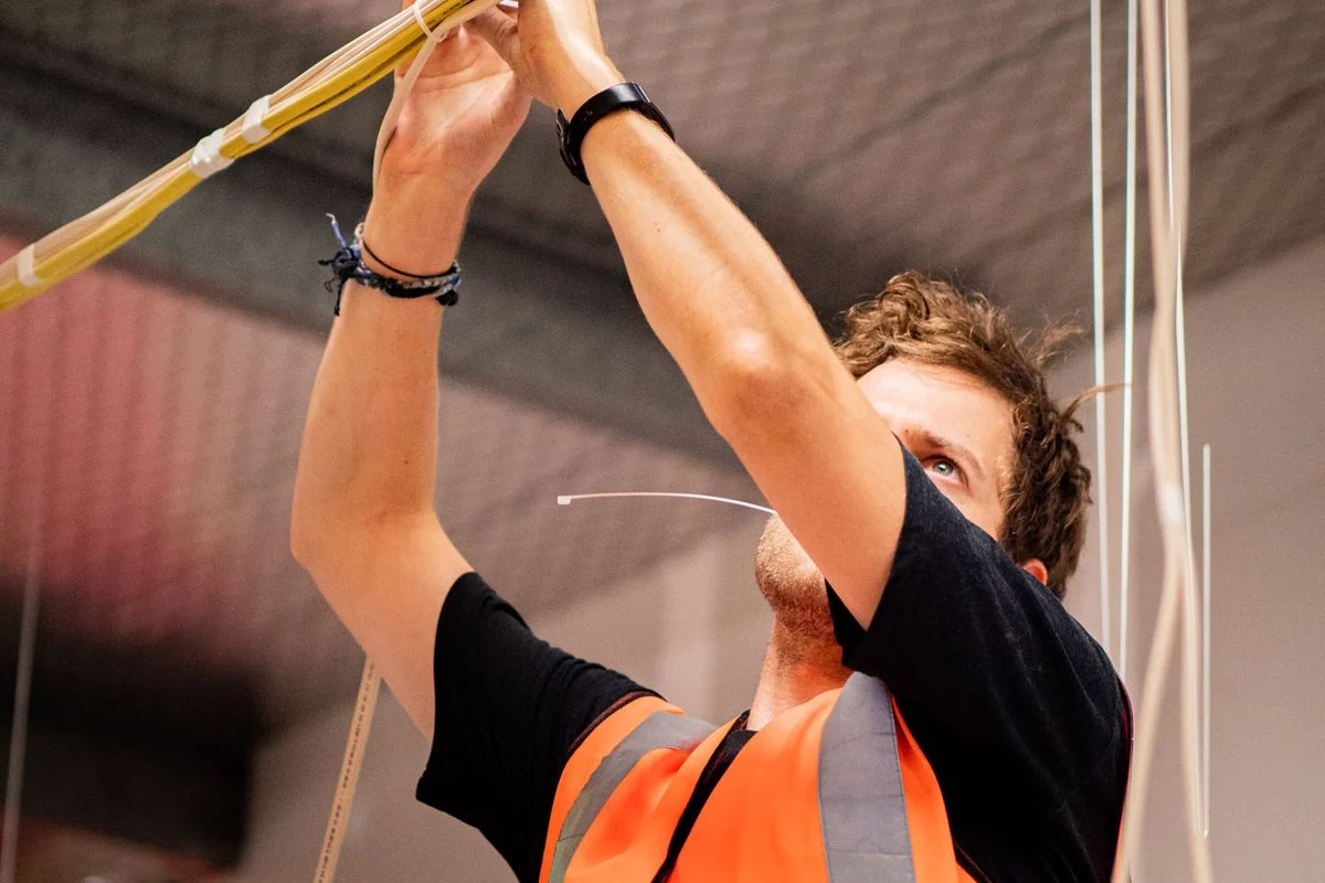 Reaching both arms overhead to run a bundle of cables along a ceiling.
