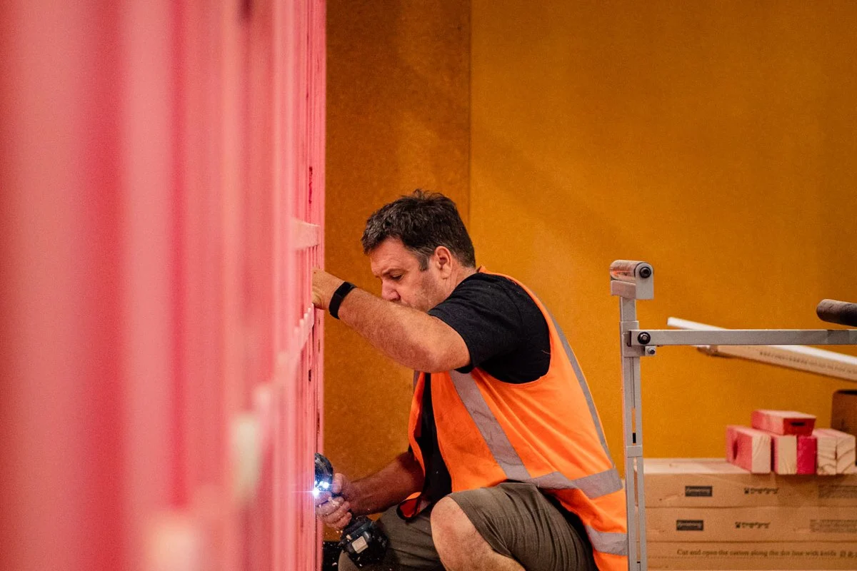 Crouched at floor level, fitting an outlet box at the base of a stud wall.