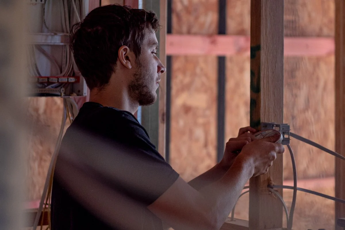 Arms raised, terminating an outlet box on a timber stud.