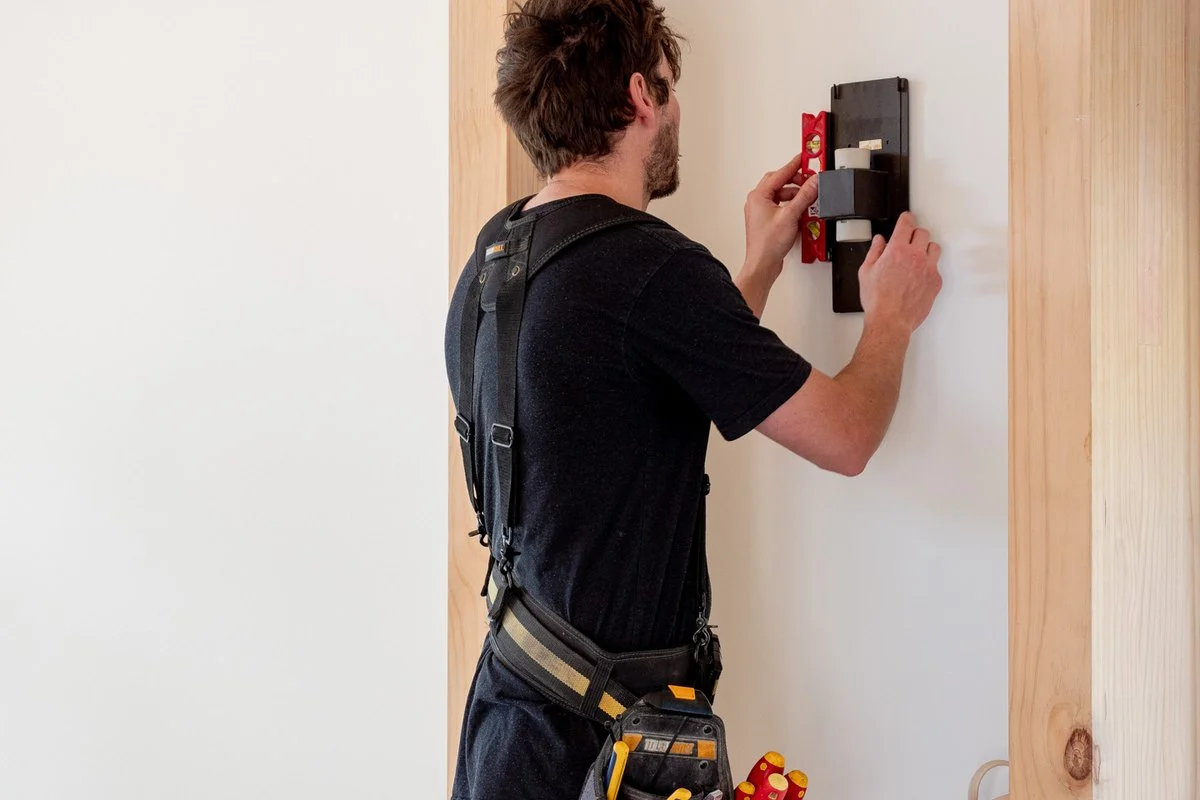 Holding a wall fitting steady with a screwdriver, side on.