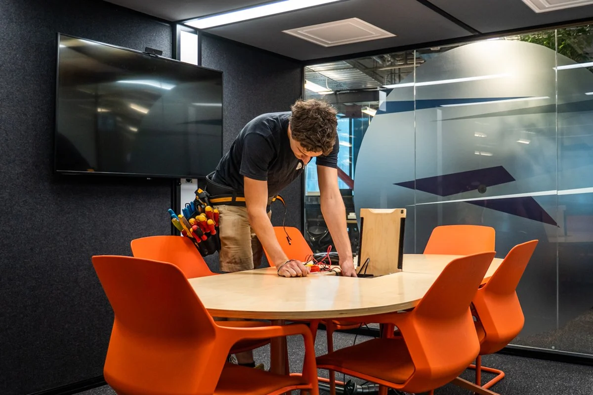 An electrician working on a power and data module set into a meeting-room table.
