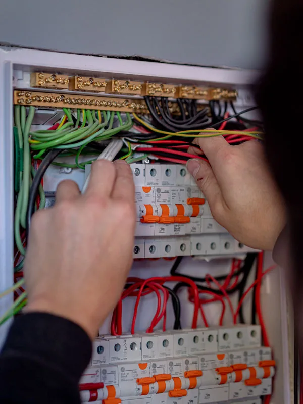 Two hands working inside a switchboard on a row of breakers with orange test buttons