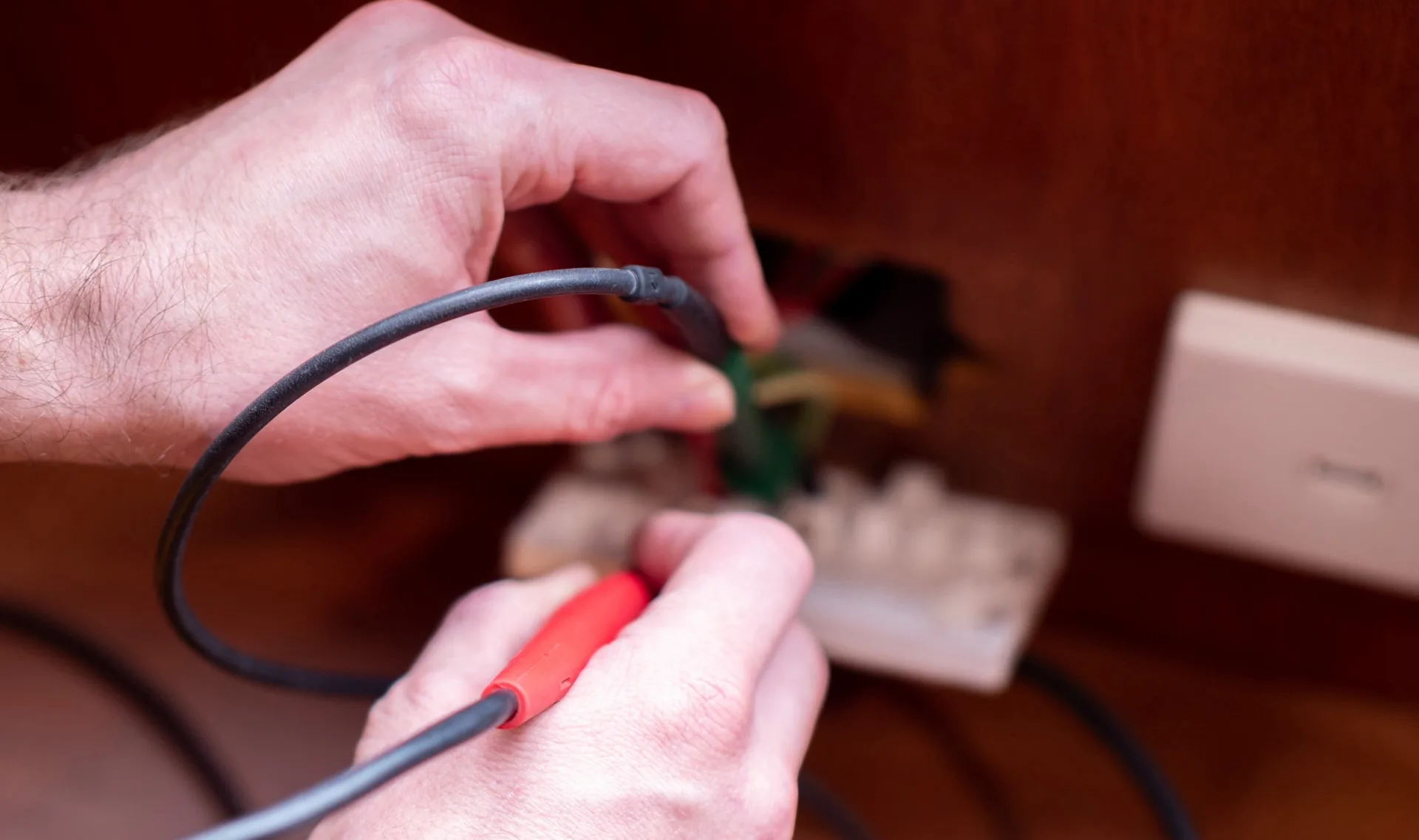 Two hands rewiring a power lead into a plug top on a wooden bench