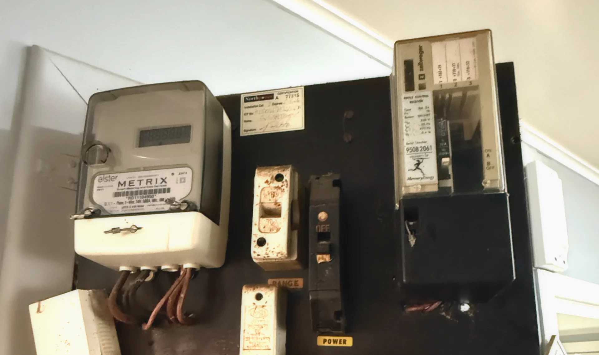 An old meter board with an electricity meter, ripple relay and ceramic fuses on a black backing