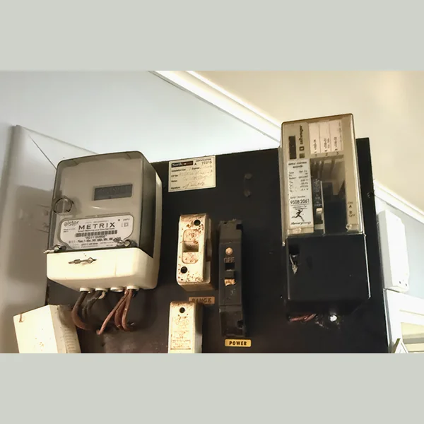An old meter board with an electricity meter, ripple relay and ceramic fuses on a black backing