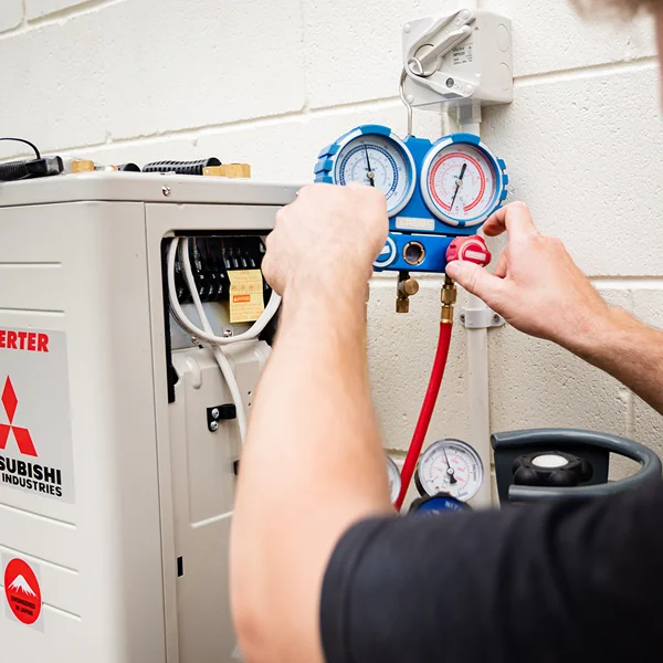 A technician connecting refrigerant gauges to an outdoor heat pump unit
