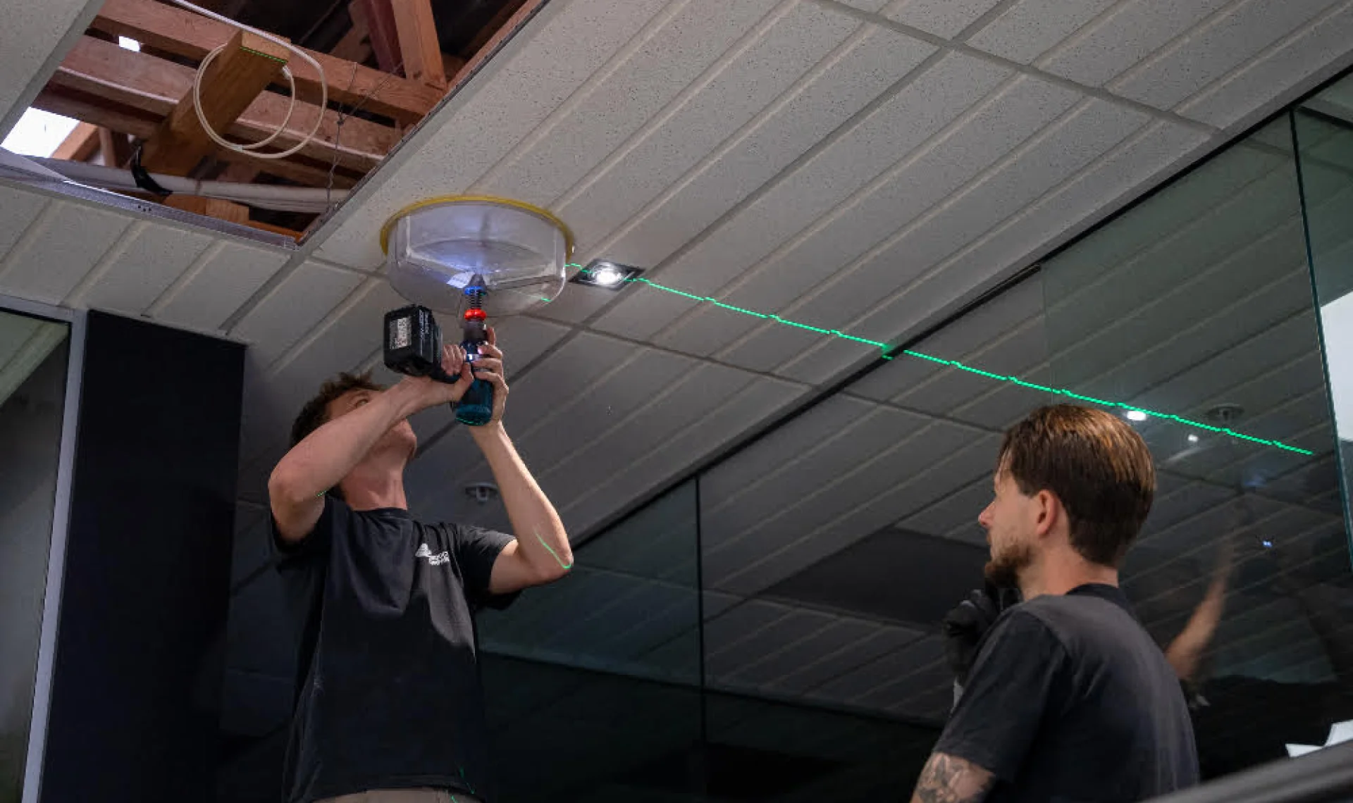 Two electricians fitting a ceiling light in an office, using a green laser level line