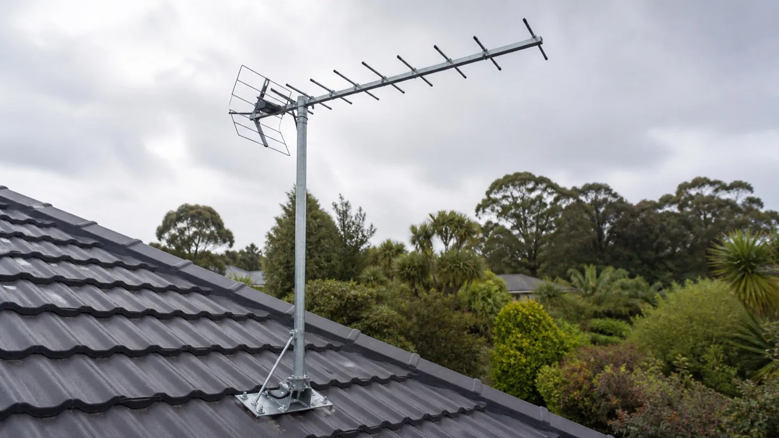 A UHF TV aerial on a mast bolted to a tiled roof, with trees behind