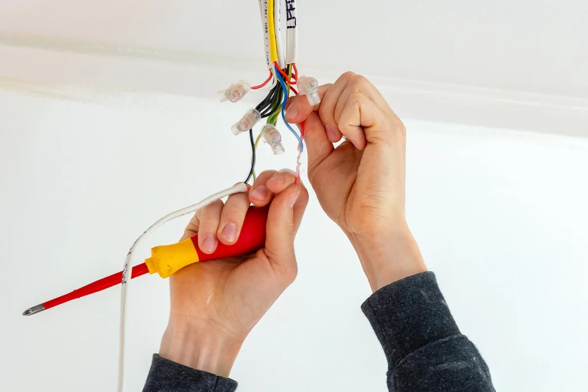 Two hands wiring a ceiling point, stripped conductors in one hand and an insulated screwdriver in the other.