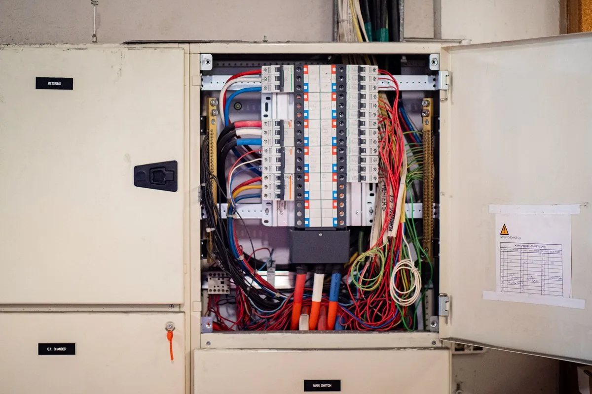 An open distribution board in a wall cabinet, with rows of circuit breakers and coloured wiring.