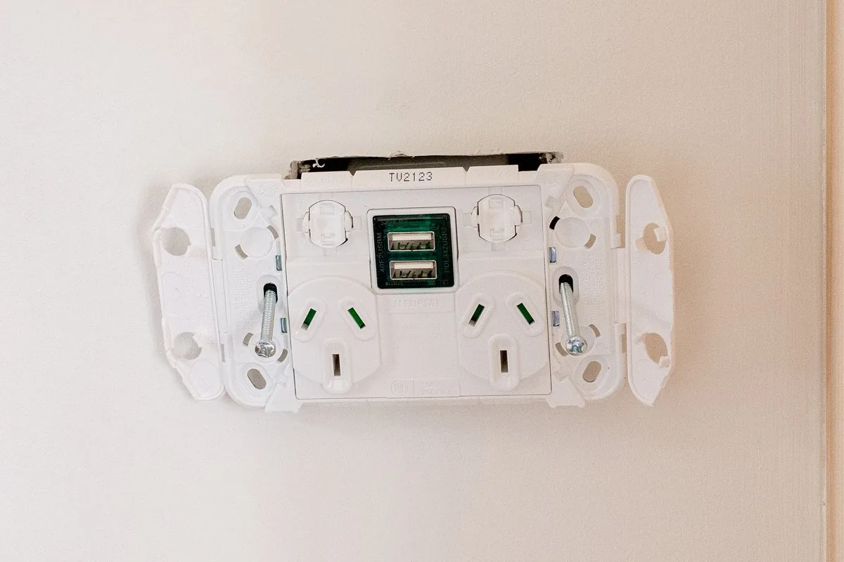 A white double power outlet with a USB port, cover off and the mechanism exposed.